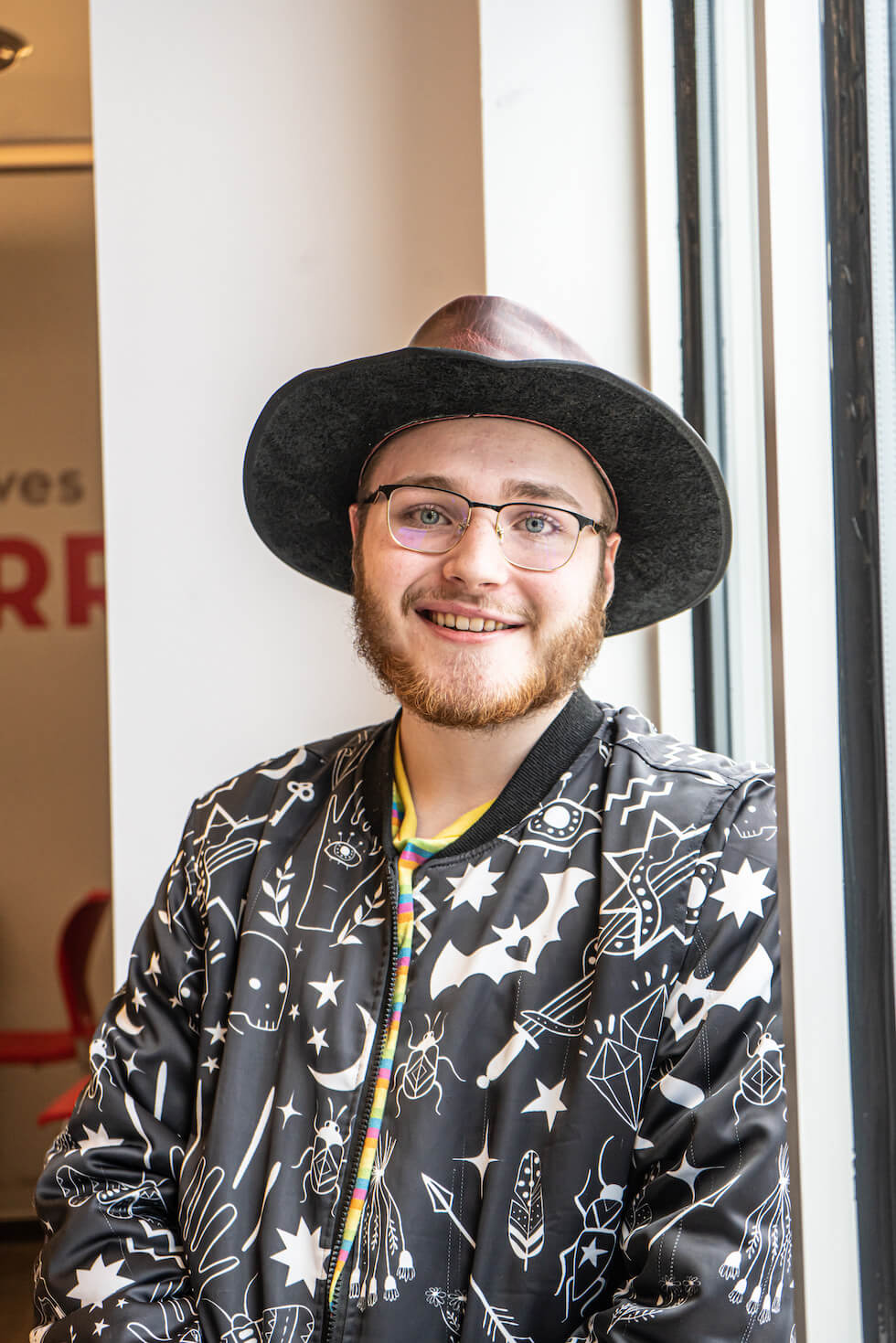 Person wearing a leather hat and graphic patterned jacket smiling.