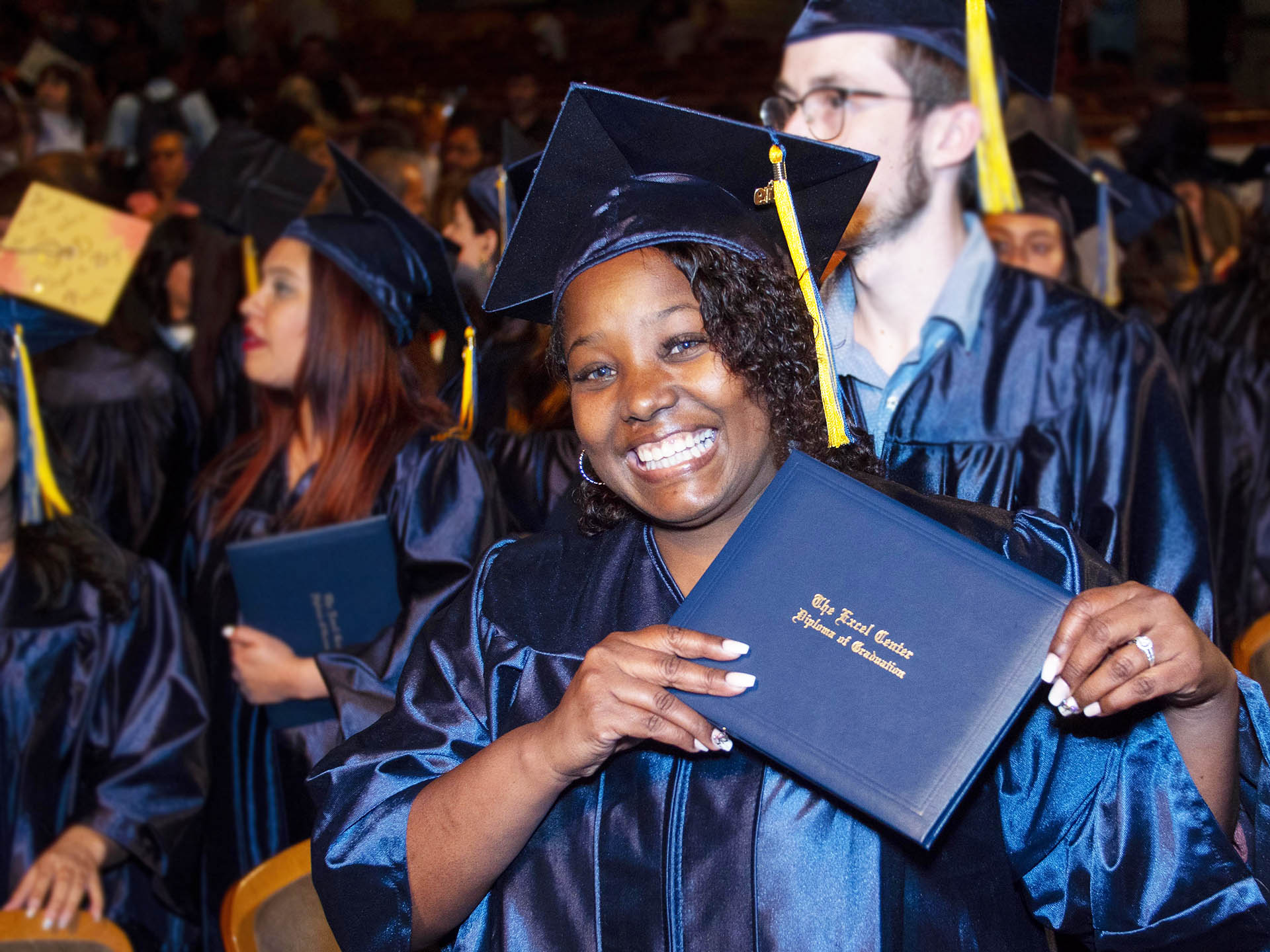 Person in graduation gown and cap smiling holding a diploma.